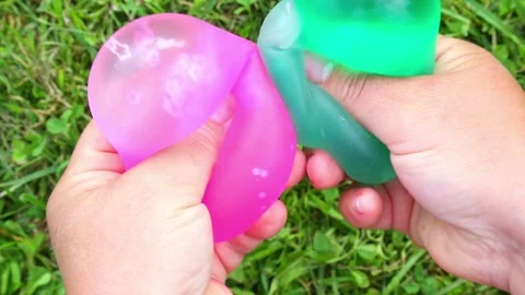 Hands squeezing colorful squishy water balloons on grass 動画素材 325623084
