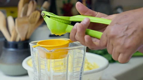 Hands squeezing fresh lime juice using a green manual press into a blender Stock Footage 339079001