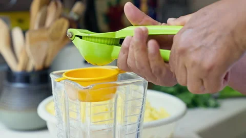 Hands squeezing fresh lime juice using a green manual press into a blender Stock Footage 341440909