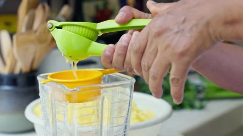 Hands squeezing fresh lime juice using a green manual press into a blender Vídeos de archivo 344988996