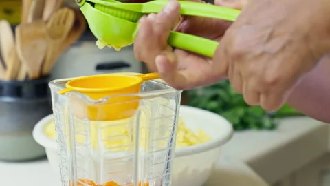 Hands squeezing fresh lime juice using a green manual press into a blender Vídeos de archivo 344989284