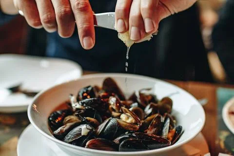 Hands squeezing lemon over plate with mussels. Stock Photos