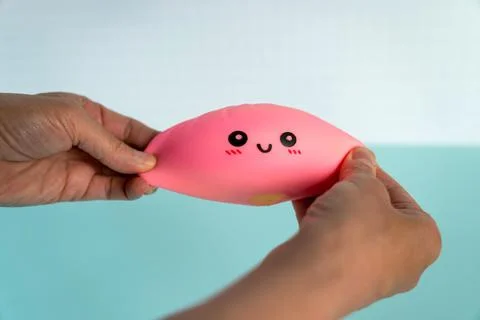 Hands squeezing a pink toy with a smiling face in a bright setting 스톡 사진