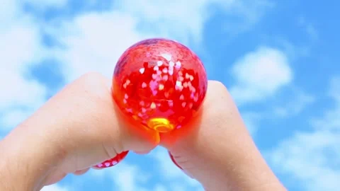 Hands squeezing red glittery stress ball against blue sky Stock Footage 319373177