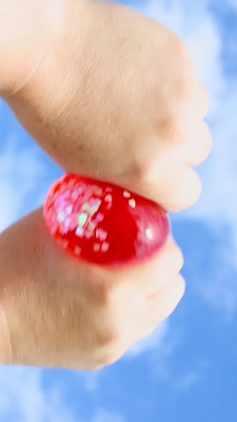 Hands squeezing red glittery stress ball against blue sky Stock Footage 322018195