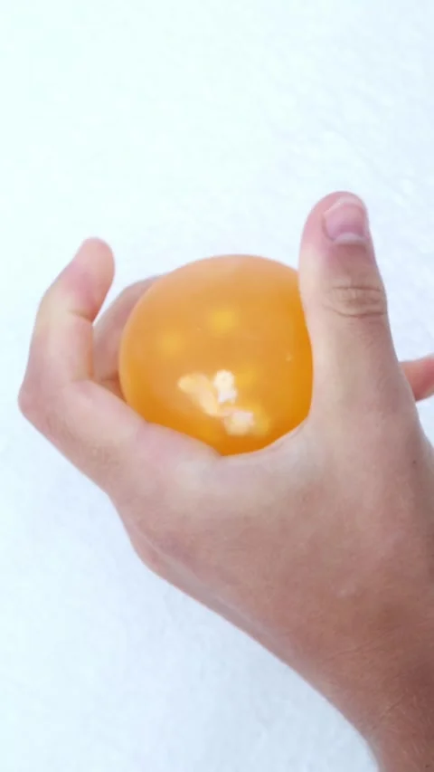 Hands squeezing yellow translucent stress ball indoors Stock Footage 321241780