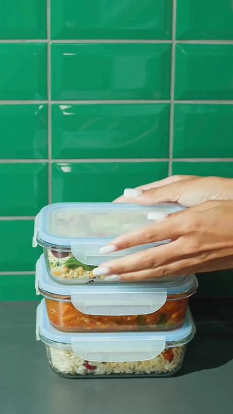 Hands stacking glass meal prep containers against green wall Video stock 331777996