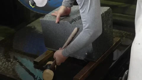 Hands steady a dark granite block on a wet workbench while a wooden mallet taps Stock-Footage 342319619