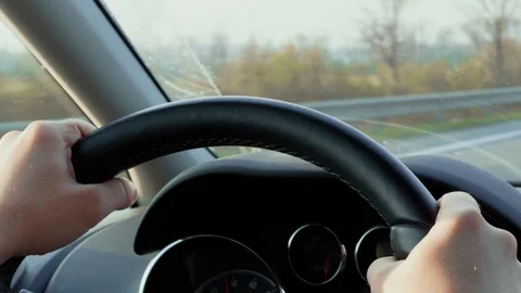 Hands on steering wheel during day driving out of town, road Stock Footage 106058190
