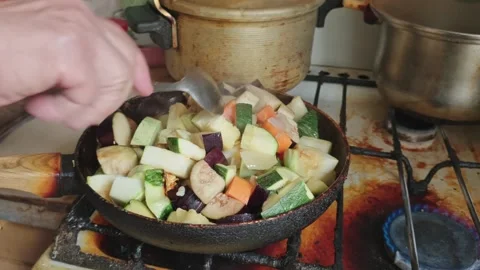 Hands stirring mixed vegetable stew in a pan on a dirty stove. Stock Footage 315226435