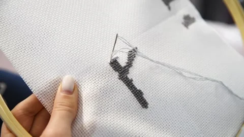 Hands stitching black cross stitch pattern on white fabric with embroidery .. Stock Footage 334955085