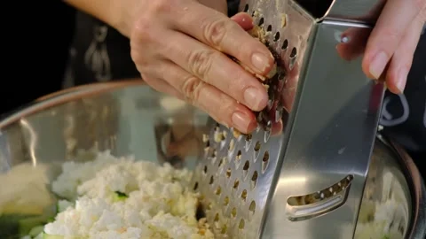 Hands straining chopped zucchini and cheese through metal sieve in Cooking Stock Footage 341416942