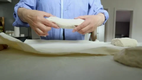 Hands stretching pale dough sheet across work surface in simple kitchen or Stock Footage 339306702