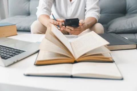 Hands studying at home with open textbook, laptop and smartphone, taking no.. 스톡 사진