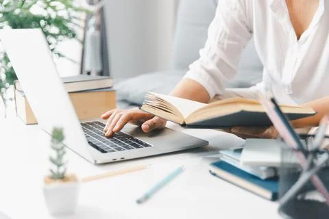 Hands studying at home, reading open book while typing on laptop on white d.. Stock Photos
