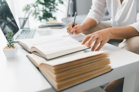 Hands studying at home, reading open textbooks while taking notes beside la.. Stock Photos