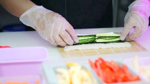 Hands sushi maker in white gloves wrapping cucumber maki roll bamboo sushi mat Stock Footage 278671313