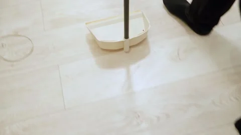 Hands sweeping floor with beige dustpan and soft bristle broom collecting debris Stock Footage 323795232