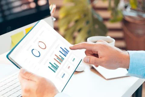 Hands on a tablet showing CRM data and graphs in a bright office workspace Stock Photos