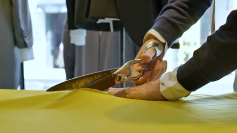 HANDS OF A TAILOR CUTTING A PIECE OF FABRIC TO MAKE A MANUFACTURED GARMENT Stock Footage 219744964