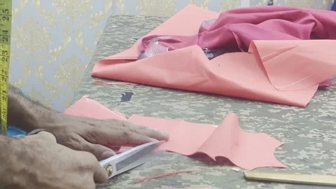 Hands of Tailor Cutting Pink Fabric with Scissors on Workshop Table Stock Footage 328973405