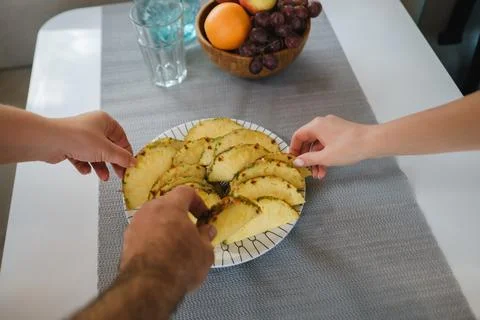 Hands take the cut pineapple on the table from the plate Stock Photos