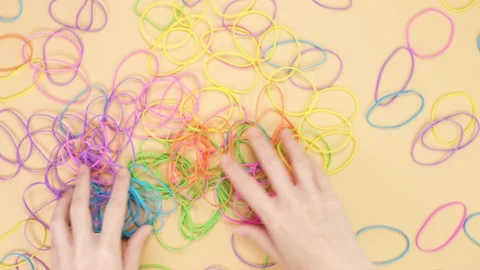 Hands taking bunch of colorful rubber bands and mix them on yellow background Stock Footage 235415677