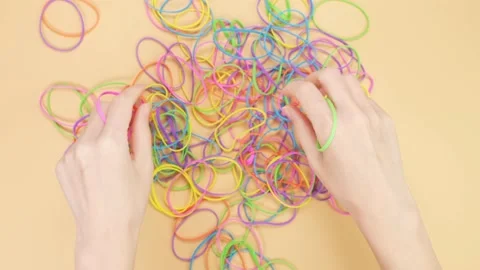 Hands taking bunch of colorful rubber bands and squizzing them on yellow Stock Footage 238426175