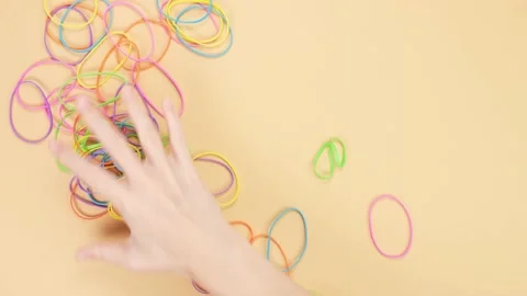 Hands taking colorful rubber bands and removing them from yellow background. Stock Footage 233375257