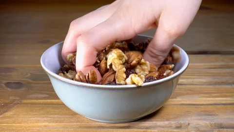 Hands taking mixed nuts and raisins from a bowl. Video stock 88170396