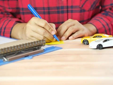 Hands taking notes in notebook with car in front. Finance and car insurance.. Stock Photos