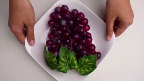 Hands taking out and putting down a plate of red grapes on table Stock Footage 274243484