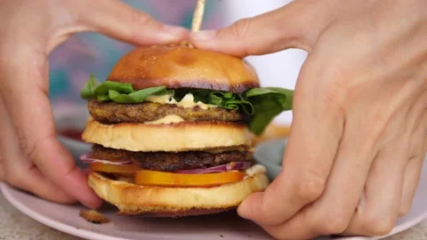 Hands taking a plant-based double-decker burger from the plate. Ketchup and Stock Footage 149671972