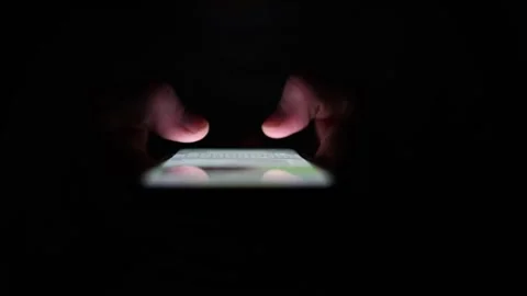 Hands tapping glowing smartphone screen in total darkness symbolizing digital ob Stock Footage 313842901