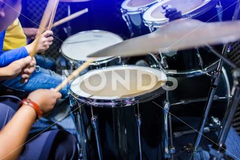 Hands of teacher with wooden drumsticks guiding boy in drum learning tutorial Stock Photos