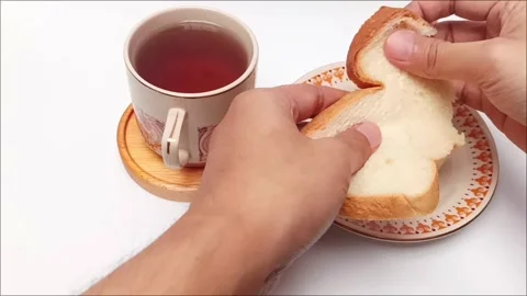 Hands tearing white bread slice beside hot black coffee cup view Stock Footage 344782760