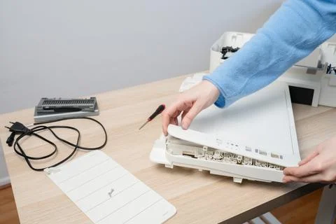 Hands of a technician disassembling a flatbed scanner printer on a wooden des Stock Photos