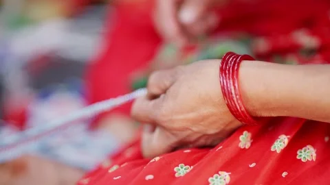 Hands thread bead string against red sari in rural Nepal Stock-Footage 342399367