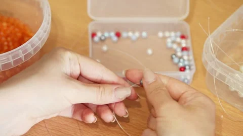 Hands threading beads with translucent thread on wooden table in natural ligh Vídeo Stock 339567174