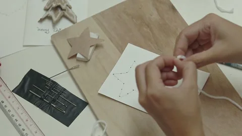 Hands threading white yarn on a big needle to be sewn into a star shape pattern Stock Footage 311423774