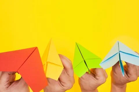 Hands throw paper planes multicolored on yellow background copy space one Stock Photos