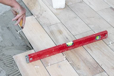 The hands of the tiler lying or installing modern, ceramic tile above cement on Stock Photos