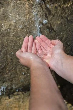 Hands together, in the foreground, taking water from a small waterfall Stock Photos