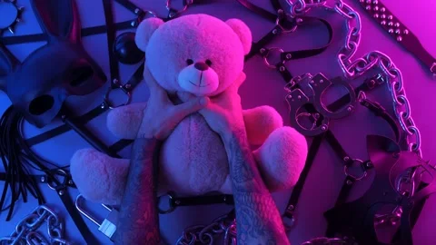 Hands touch a toy bear on the table with a BDSM accessory whips chains masks for Stock Footage 144666075