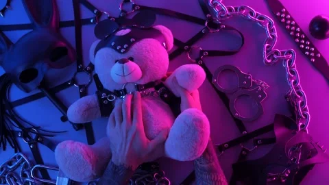 Hands touch a toy bear on the table with a BDSM accessory whips chains masks for Stock Footage 144666764