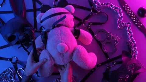 Hands touch a toy bear on the table with a BDSM accessory whips chains masks for Stock Footage 144667036