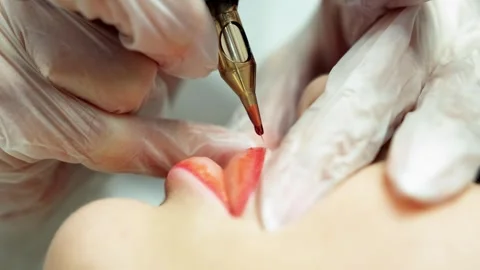 Hands in transparent gloves hold a machine for permanent female lip tattooing Stockbeeldmateriaal 264059039
