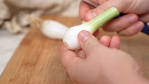 Hands trimming roots from a spring onion bulb with a knife on a bamboo cutt.. Stock Footage 347182057