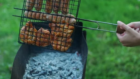 Hands turn grill grate with roasted chicken thighs. Grilling sausages meat on Stock Footage 251738469
