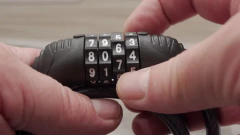 Hands turn the plastic wheels on the combination cable lock to set the numbers. Stock Footage 320889508